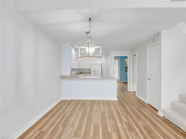 Kitchen with white refrigerator with ice dispenser, wood-type flooring, kitchen peninsula, a chandelier, and white cabinets