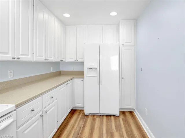 Kitchen featuring light wood-type flooring, white fridge with ice dispenser, and white cabinets
