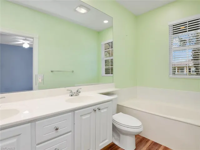Bathroom with hardwood / wood-style flooring, toilet, a tub, ceiling fan, and vanity