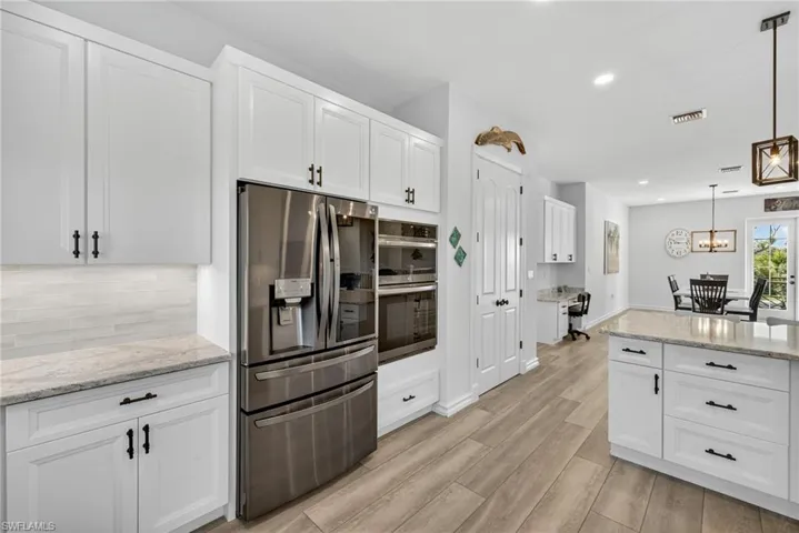 Kitchen featuring stainless steel appliances, light stone countertops, white cabinetry, decorative light fixtures, and recessed lighting