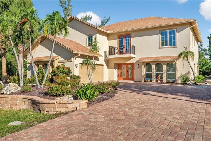 View of front of home featuring a balcony, french doors, decorative driveway, stucco siding, and a garage