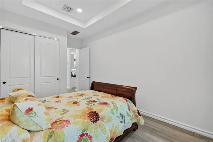Bedroom with light wood finished floors, a closet, a raised ceiling, and recessed lighting