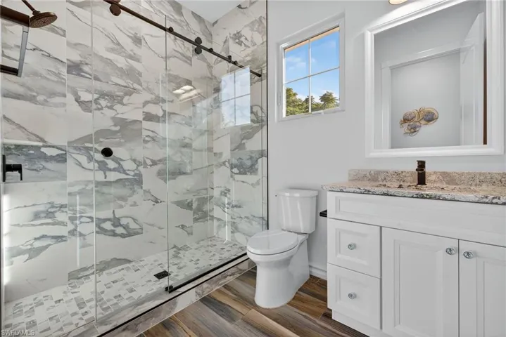 Bathroom featuring a marble finish shower, vanity, and dark wood finished floors