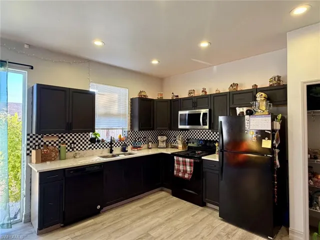 Kitchen featuring black appliances, light wood-style floors, dark cabinets, recessed lighting, and tasteful backsplash