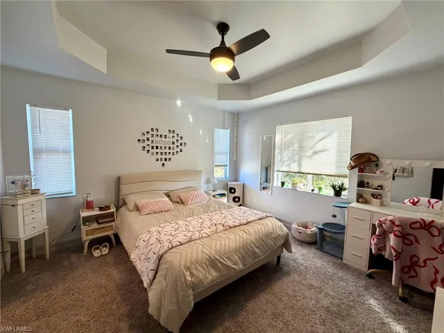 Carpeted bedroom featuring a tray ceiling and a ceiling fan
