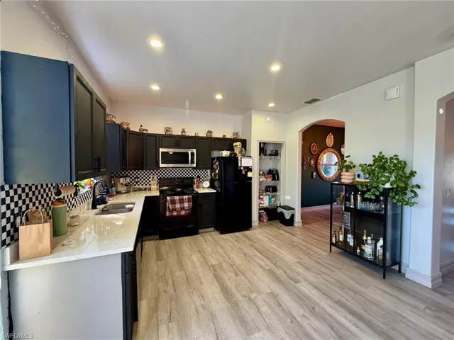Kitchen featuring arched walkways, light stone counters, black appliances, tasteful backsplash, and light wood-style floors