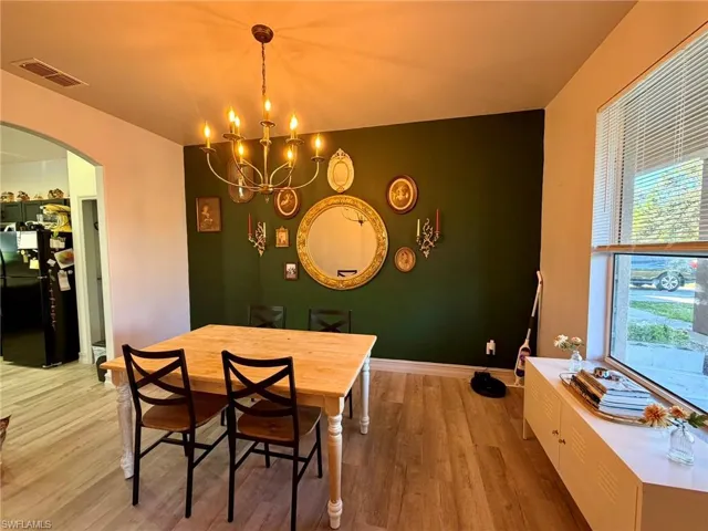 Dining space with wood finished floors, arched walkways, a chandelier, and an accent wall