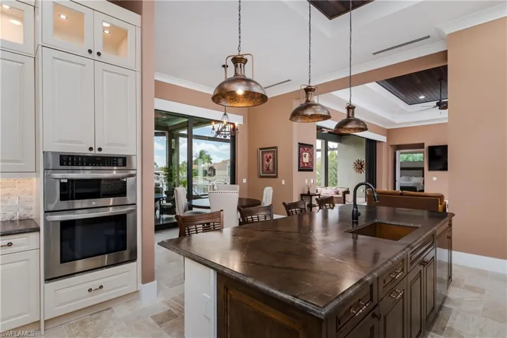 Kitchen featuring stainless steel appliances, a center island with sink, a raised ceiling, glass insert cabinets, and crown molding