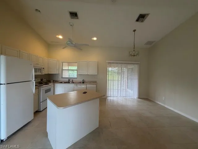 Open-concept kitchen and dining area featuring vaulted ceilings, a central kitchen island, white cabinetry, and a sliding glass door with vertical blinds