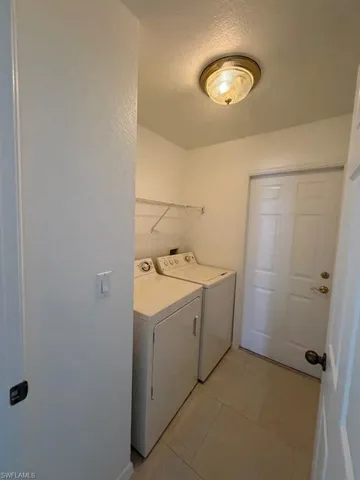 Dedicated laundry room featuring side-by-side washer and dryer hookups, tile flooring, abundant counter space with upper cabinetry, ceiling-mounted light fixture, and direct access to additional living areas