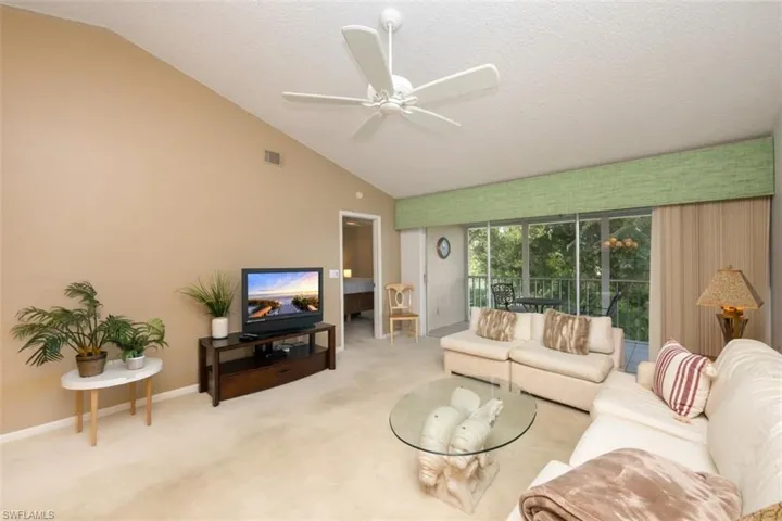 Living area with lofted ceiling, carpet floors, a textured ceiling, a sunroom, and a ceiling fan
