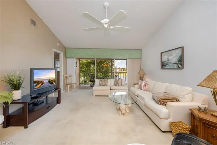 Living area with carpet floors, ceiling fan, and high vaulted ceiling