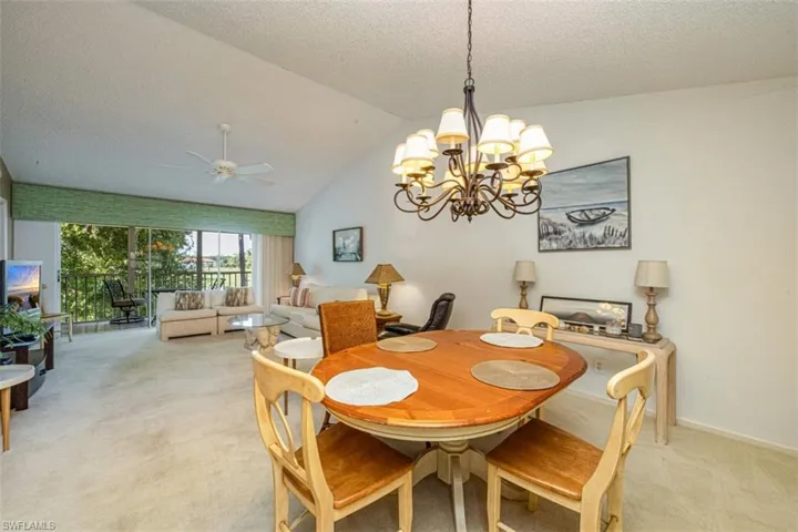 Dining area featuring light colored carpet, vaulted ceiling, a ceiling fan, a chandelier, and a textured ceiling