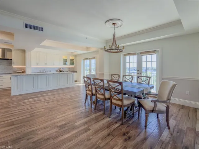 Dining space featuring light wood-type flooring, a raised ceiling, hanging lights, french doors, and crown molding