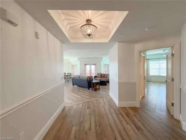 Corridor with crown molding, light wood-type flooring, a raised ceiling, and hanging lights