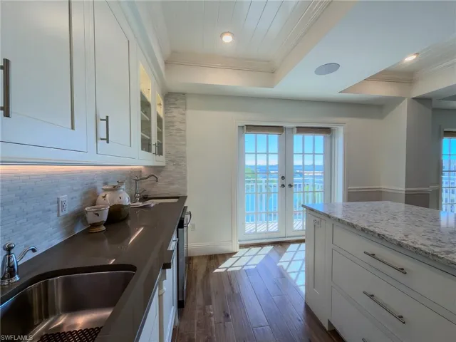 Kitchen with white cabinetry, dark wood-type flooring, french doors, ornamental molding, and dark stone counters