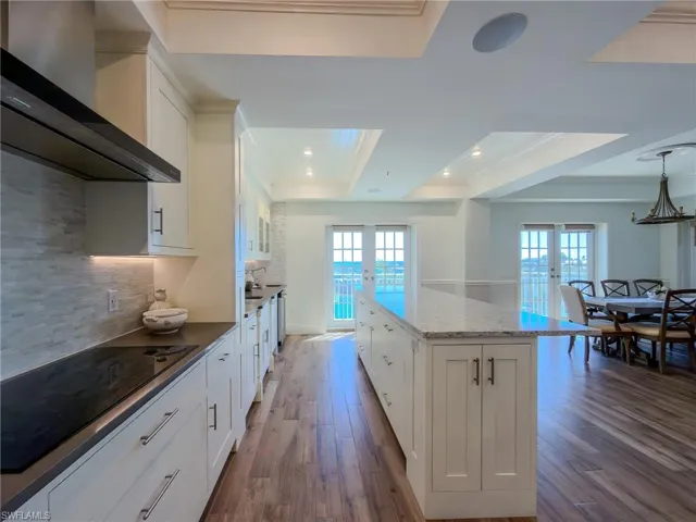 Kitchen with white cabinetry, black electric stovetop, dark wood-type flooring, a center island, and a tray ceiling