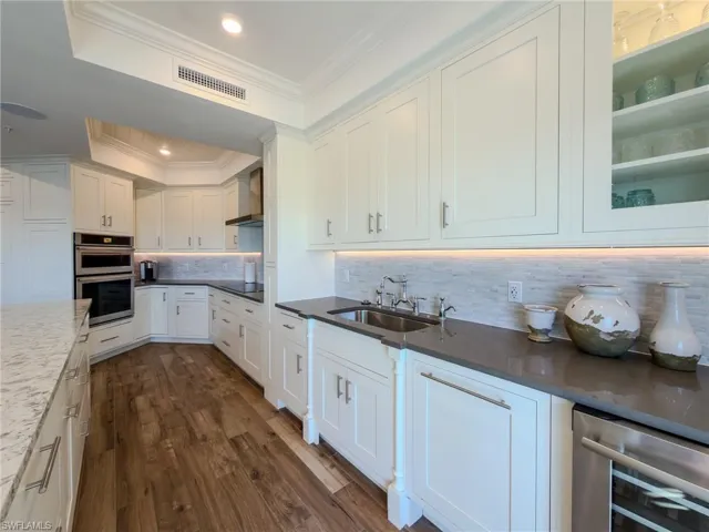 Kitchen featuring white cabinetry, backsplash, dark wood-type flooring, stainless steel double oven, and dark stone counters
