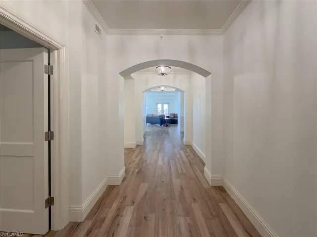 Corridor featuring crown molding, light wood-type flooring, and arched walkways