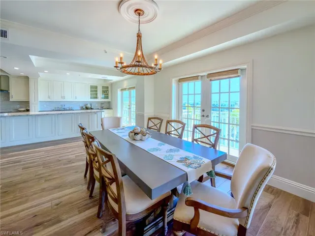 Dining space with light wood-style floors, french doors, suspended lighting, a raised ceiling, and healthy amount of natural light