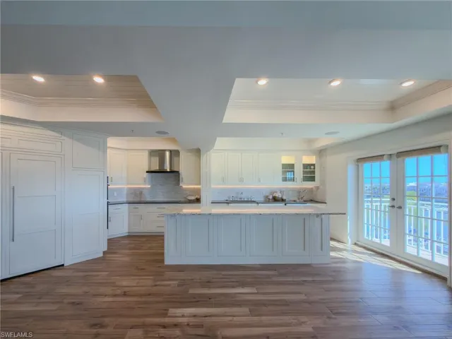 Kitchen with a raised ceiling, white cabinetry, ornamental molding, decorative backsplash, and dark wood-type flooring