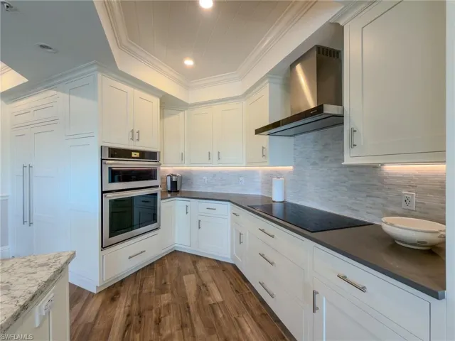 Kitchen with dark wood finished floors, white cabinets, stainless steel double oven, ornamental molding, and backsplash