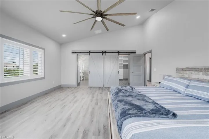 Bedroom featuring light wood-type flooring, a barn door, vaulted ceiling, and ceiling fan