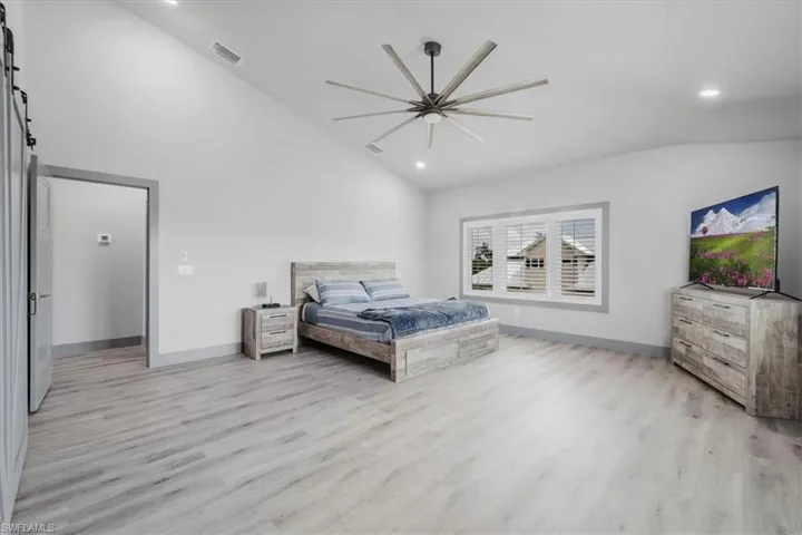 Bedroom featuring light hardwood / wood-style flooring, a barn door, ceiling fan, and high vaulted ceiling