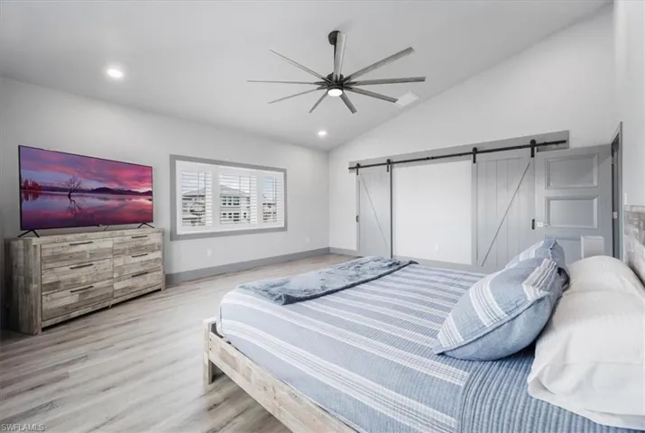 Bedroom featuring ceiling fan, a barn door, light hardwood / wood-style flooring, and vaulted ceiling