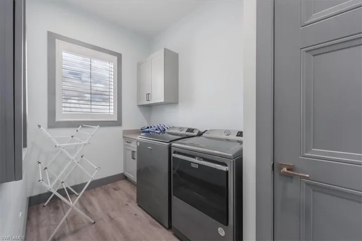 Clothes washing area with cabinets, washing machine and clothes dryer, and light hardwood / wood-style floors