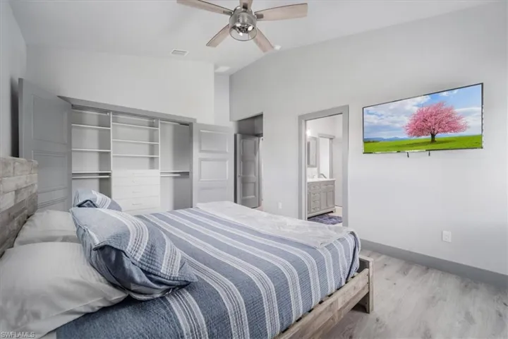 Bedroom featuring lofted ceiling, ensuite bath, a closet, ceiling fan, and hardwood / wood-style floors