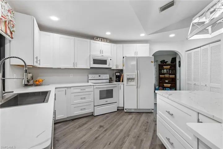 Kitchen with white appliances, sink, vaulted ceiling, light stone countertops, and white cabinetry