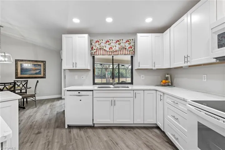 Kitchen featuring white cabinetry, sink, pendant lighting, and white appliances
