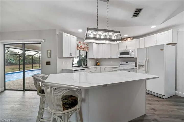 Kitchen with white cabinetry, sink, lofted ceiling, white appliances, and a kitchen island