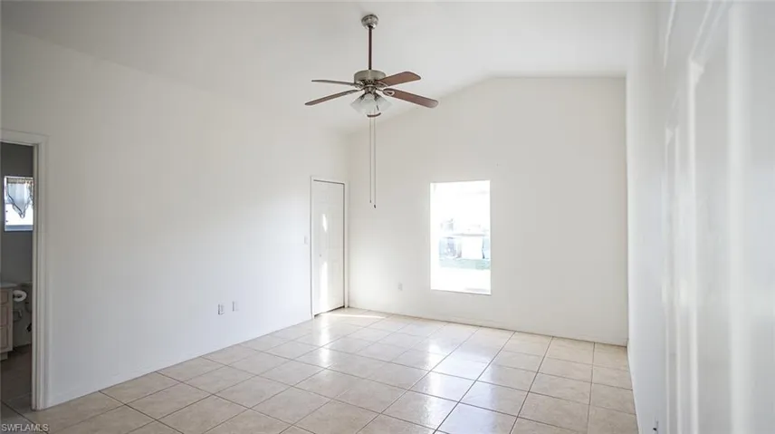 Unfurnished room with lofted ceiling, ceiling fan, and light tile patterned floors