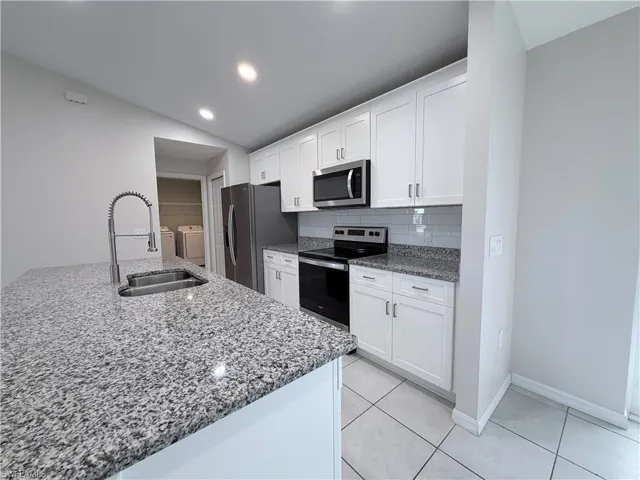 Kitchen with light stone countertops, white cabinetry, stainless steel appliances, independent washer and dryer, and backsplash