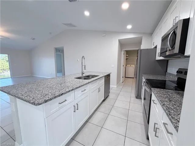 Kitchen featuring stainless steel appliances, white cabinets, light stone countertops, light tile patterned flooring, and lofted ceiling