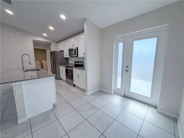 Kitchen featuring light stone countertops, stainless steel appliances, washing machine and dryer, white cabinetry, and vaulted ceiling