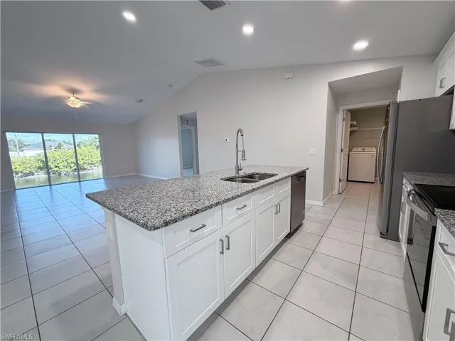 Kitchen with white cabinetry, stainless steel appliances, light tile patterned floors, washer / clothes dryer, and light stone counters