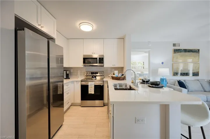 Kitchen with sink, stainless steel appliances, white cabinets, decorative backsplash, and kitchen peninsula