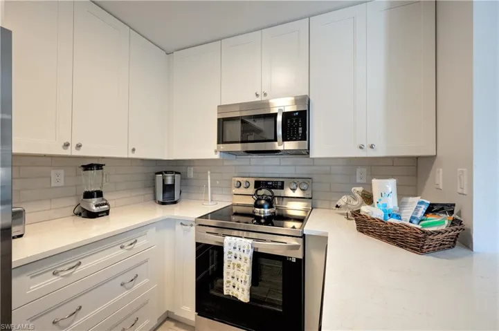 Kitchen with backsplash, appliances with stainless steel finishes, light stone counters, and white cabinets
