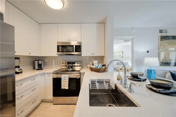 Kitchen featuring stainless steel appliances, sink, decorative backsplash, and white cabinets