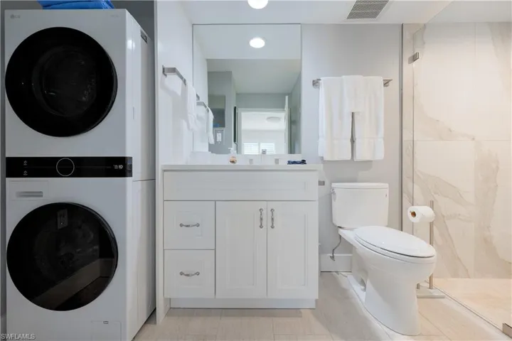 Bathroom featuring vanity, stacked washer / drying machine, toilet, and a shower