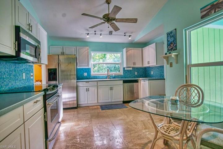 Updated kitchen featuring corian countertops, galss tile backsplash, custom lighting, white wood cabinetry, natural stone flooring, a walk-in pantry and stainless steel appliances.