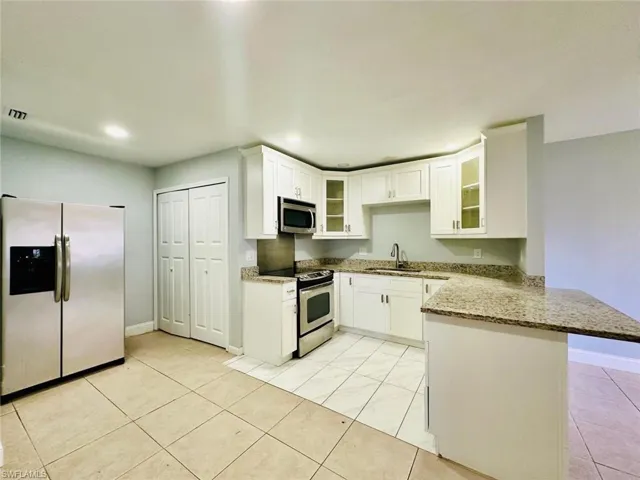 Kitchen featuring stainless steel appliances, glass fronted cabinets, light stone countertops, a peninsula, and white cabinetry