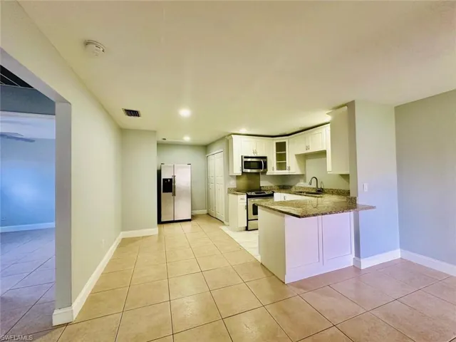 Kitchen featuring dark stone counters, glass insert cabinets, a peninsula, stainless steel appliances, and white cabinetry