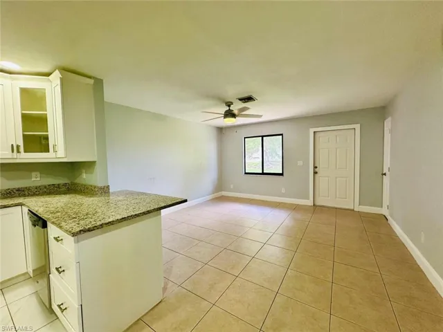 Kitchen featuring white cabinets, light stone counters, glass fronted cabinets, dishwashing machine, and open floor plan