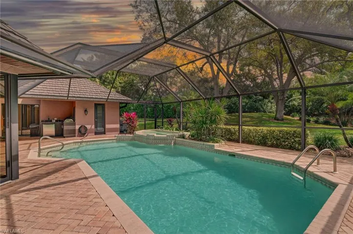 Pool at dusk featuring a lanai, a sunroom, a pool with connected hot tub, and a patio