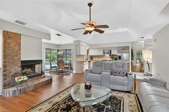 Living room with wood-type flooring, a ceiling fan, a brick fireplace, and recessed lighting