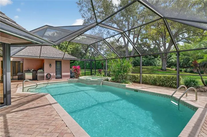 Combined pool / hot tub with glass enclosure, a patio, a sunroom, and area for grilling